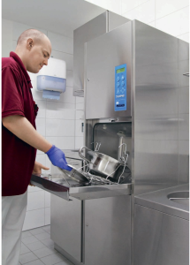 A person loads pots and pans into a commercial bedpan washer in a room setting.