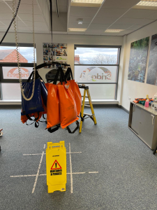 A ceiling hoist displaying orange bags suspended from it, indicating weight measurement.