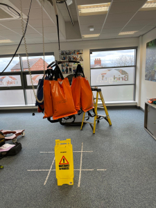 A ceiling hoist displaying orange bags suspended from it, indicating weight measurement.