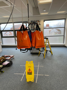 A ceiling hoist displaying orange bags suspended from it, indicating weight measurement.