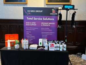 Exhibit table displaying cleaning and sanitizing products, promotional materials, and equipment beneath a "Total Service Solutions" banner from 24 NRG Group and Trade Care.